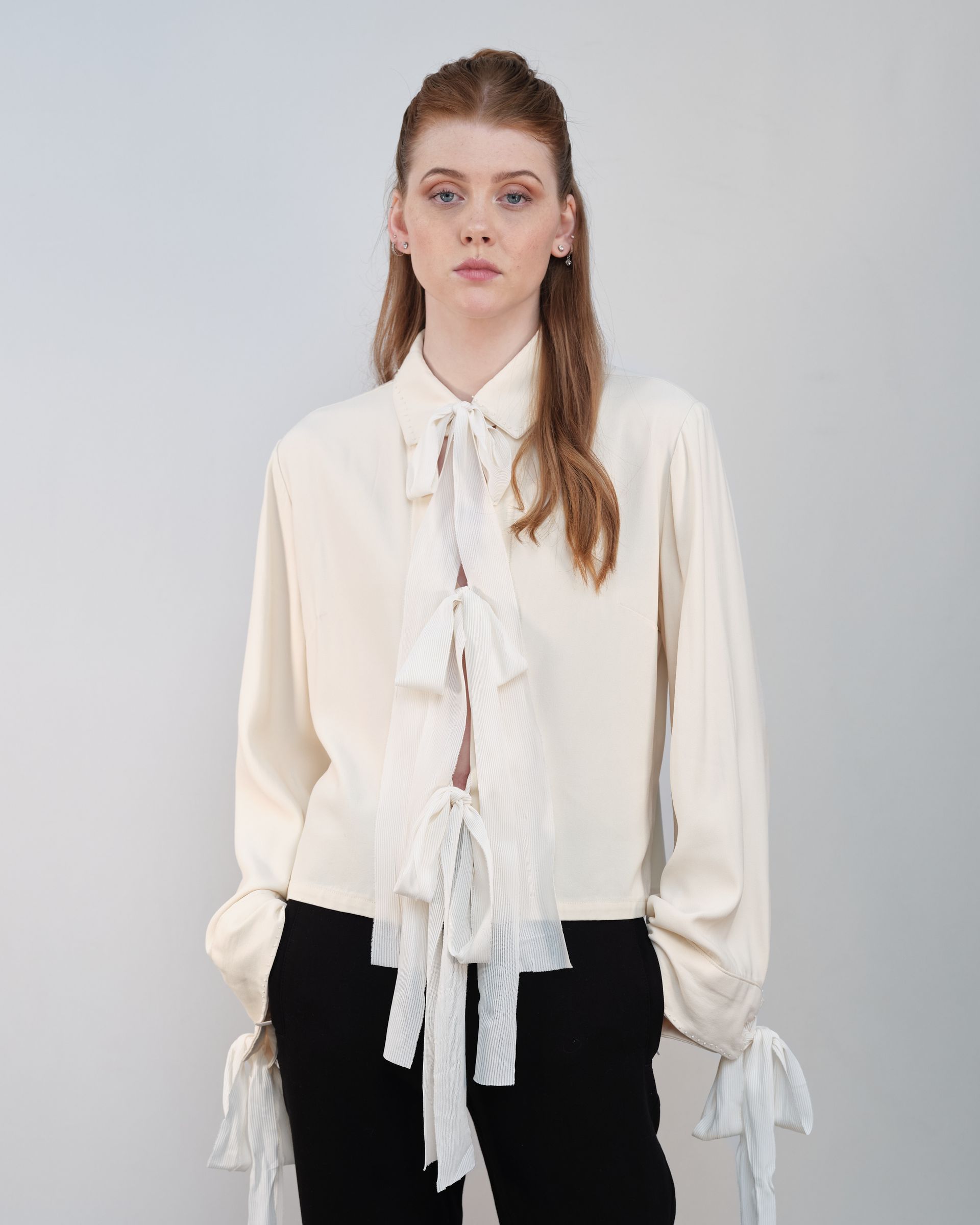 A woman is wearing a white shirt with ruffles and black pants.