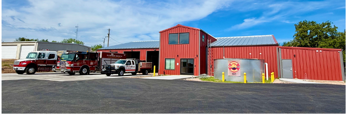 Red fire station with parked fire trucks and a bay door on a sunny day