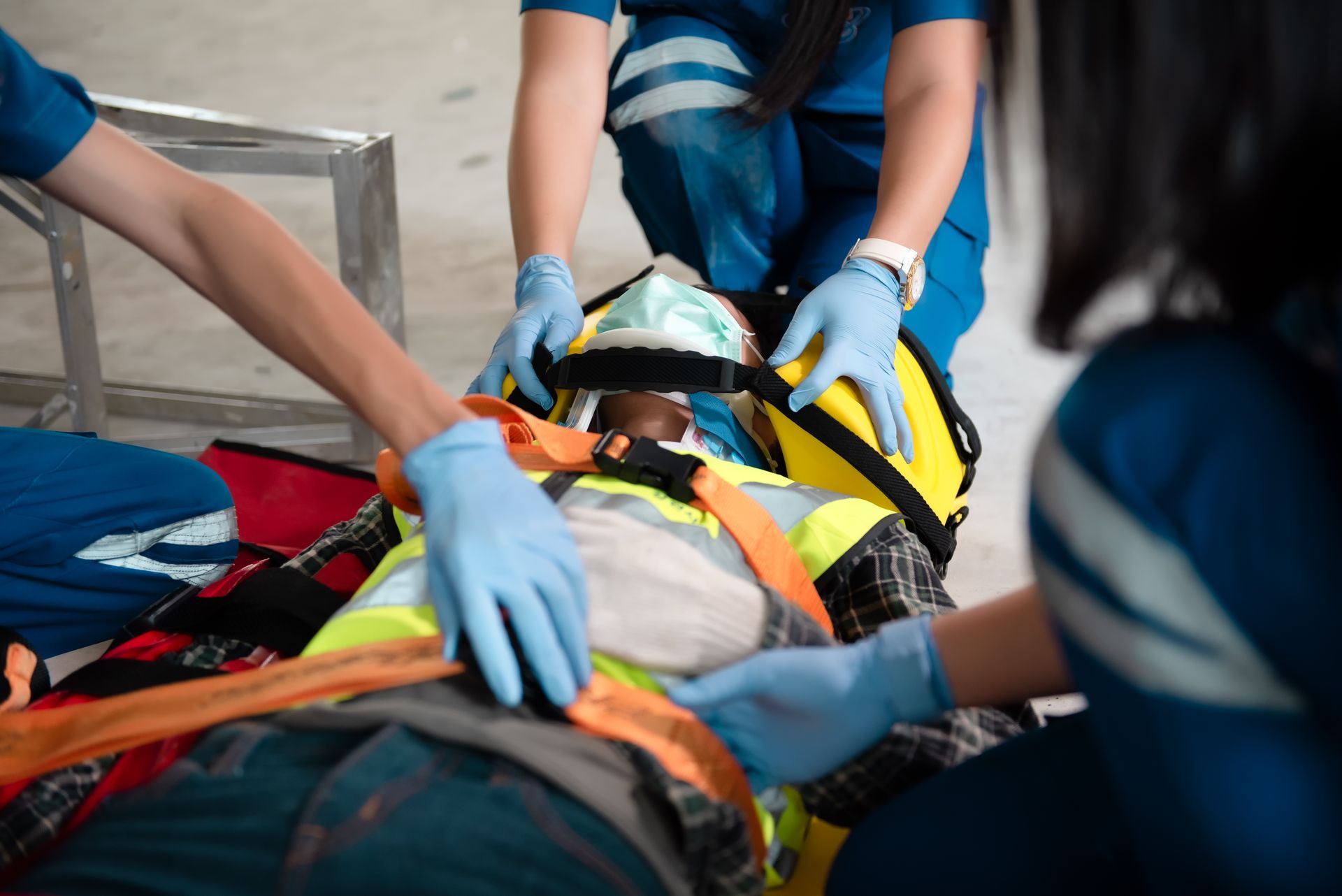 Emergency medical personnel tending to a person on a stretcher, securing their head and torso with straps, indoors.