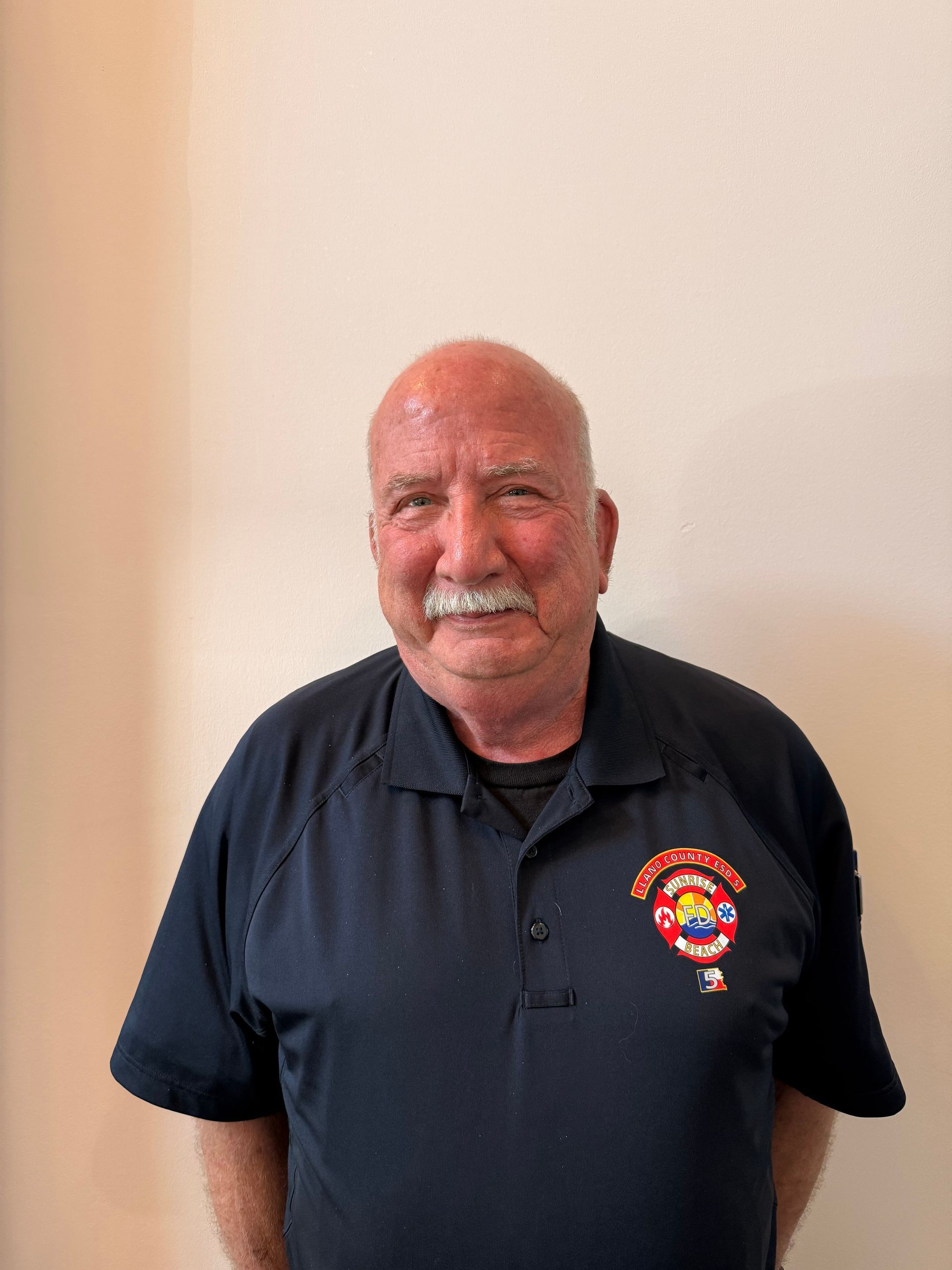 Smiling man in navy polo shirt standing against a beige wall