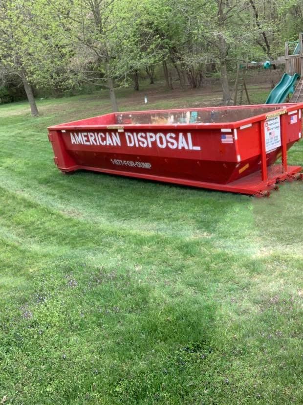 A fifteen cubic yard red dumpster is parked in a lawn.