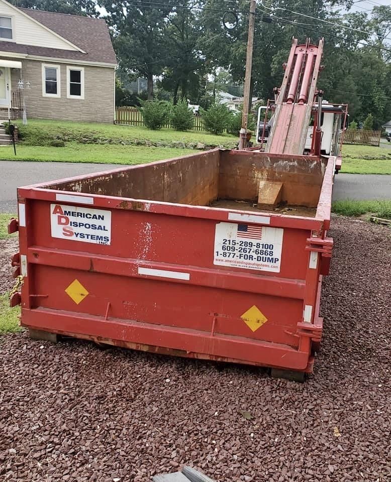 A red, twenty cubic yard dumpster is parked on a stone driveway