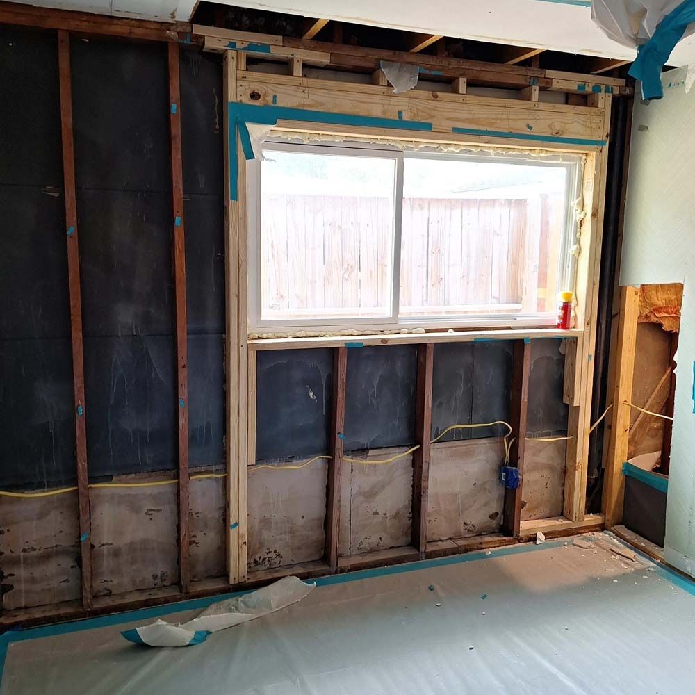 Unfinished interior wall with exposed framing and insulation around a window.