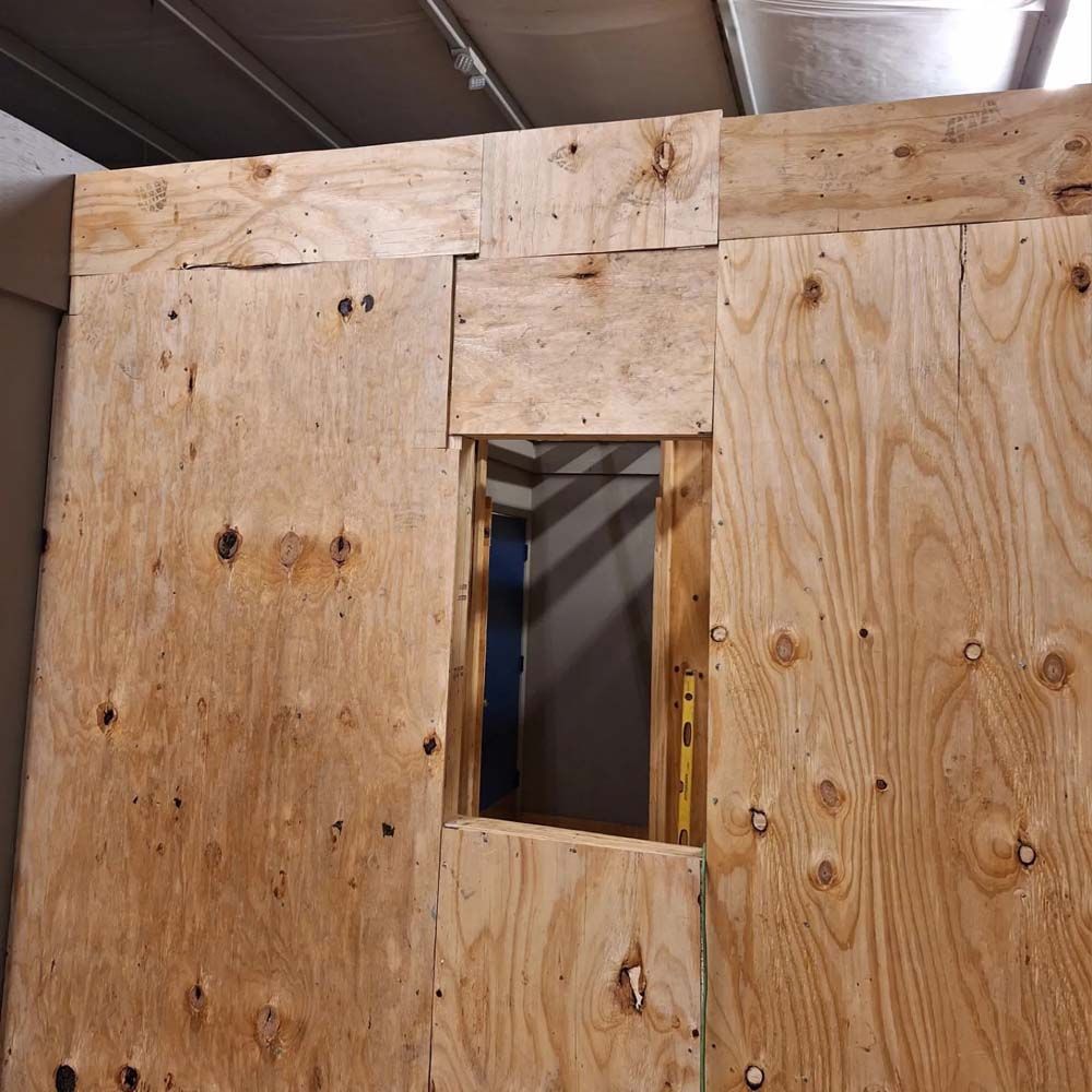 Plywood wall with a small rectangular window opening in an indoor construction area