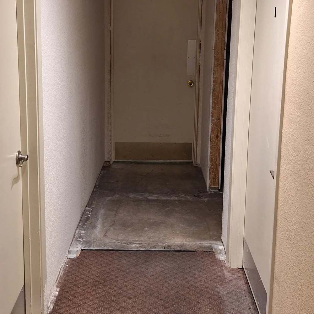 Narrow hallway with worn flooring and a small step leading to a closed door.