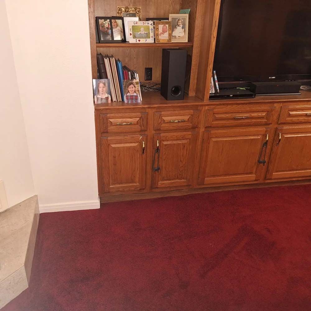 Living room corner with wooden TV cabinet, shelves, and red carpeted floor