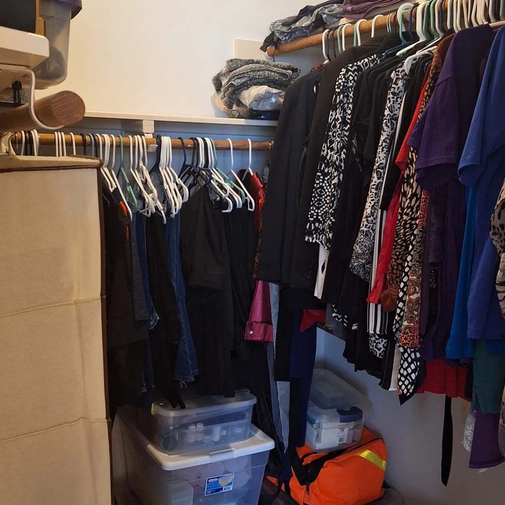 Cluttered walk-in closet with hanging clothes, plastic storage bins, and folded items on shelves.
