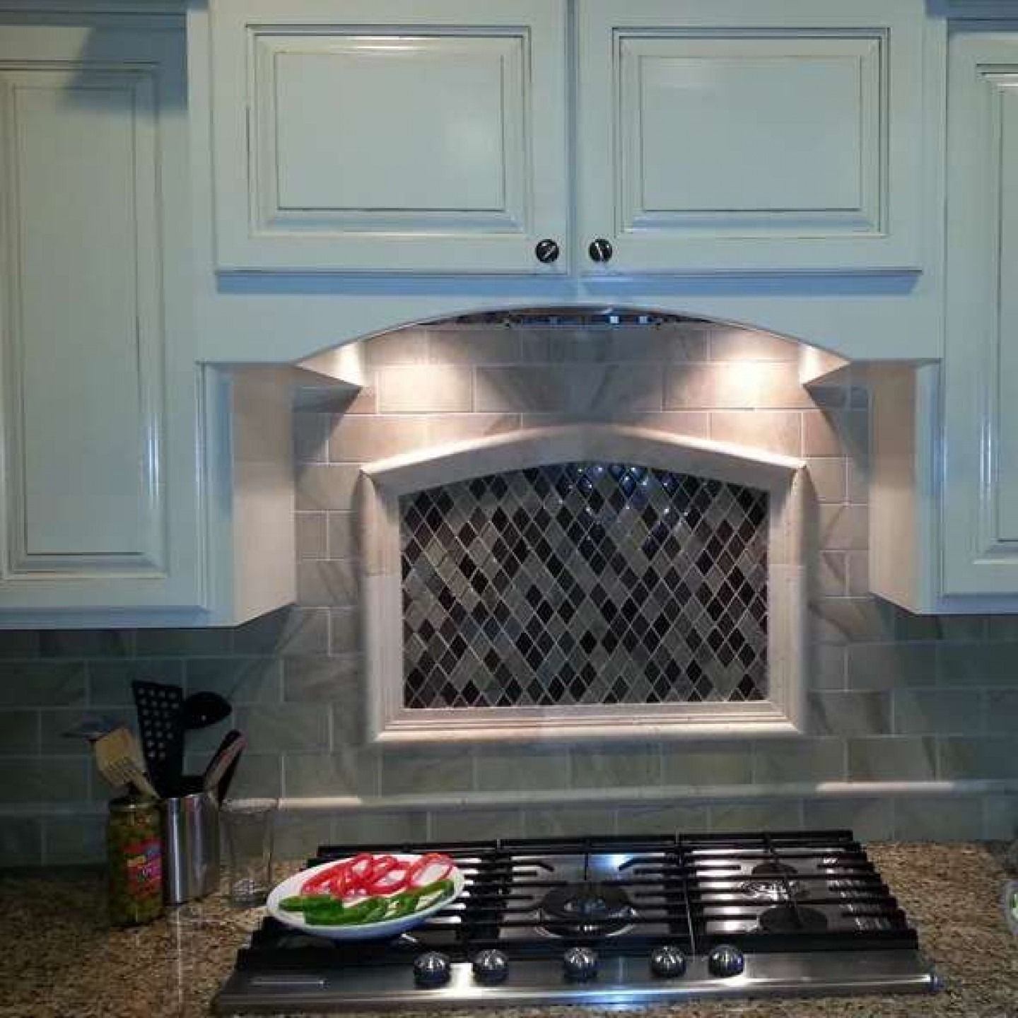Kitchen stove with a plate of sliced vegetables and a backsplash under a lit range hood