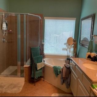 Modern bathroom with glass shower, corner tub, sink, and towels by a window