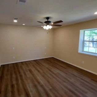 Empty beige room with wood-look flooring, ceiling fan, and a window on the right.