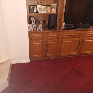 Living room with red carpet, wooden cabinets, bookshelf, and a TV cabinet.
