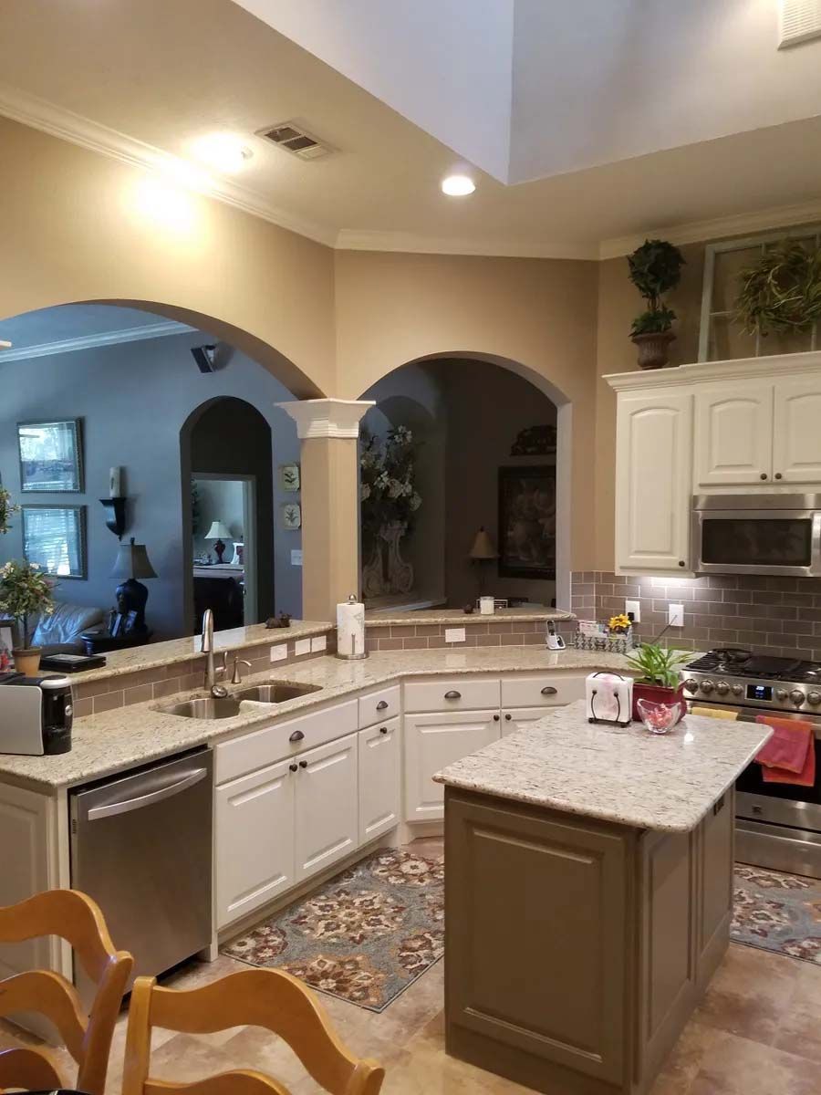Bright kitchen with white cabinets, granite island, arched doorways, and recessed lighting