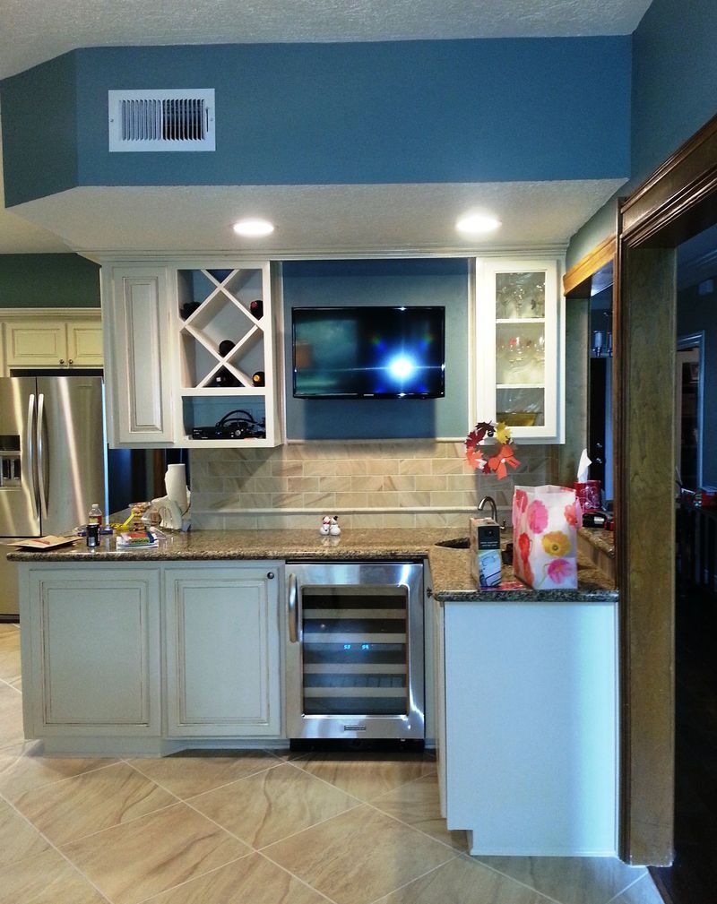 Modern kitchen with light cabinets, granite counter, built-in TV, and stainless steel oven in a blue-accented wall.