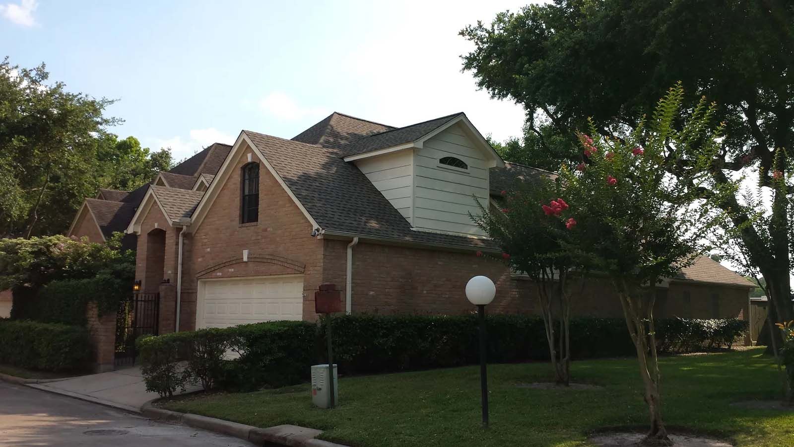 Suburban brick house with gabled roof, trees, and a front lawn beside a quiet street