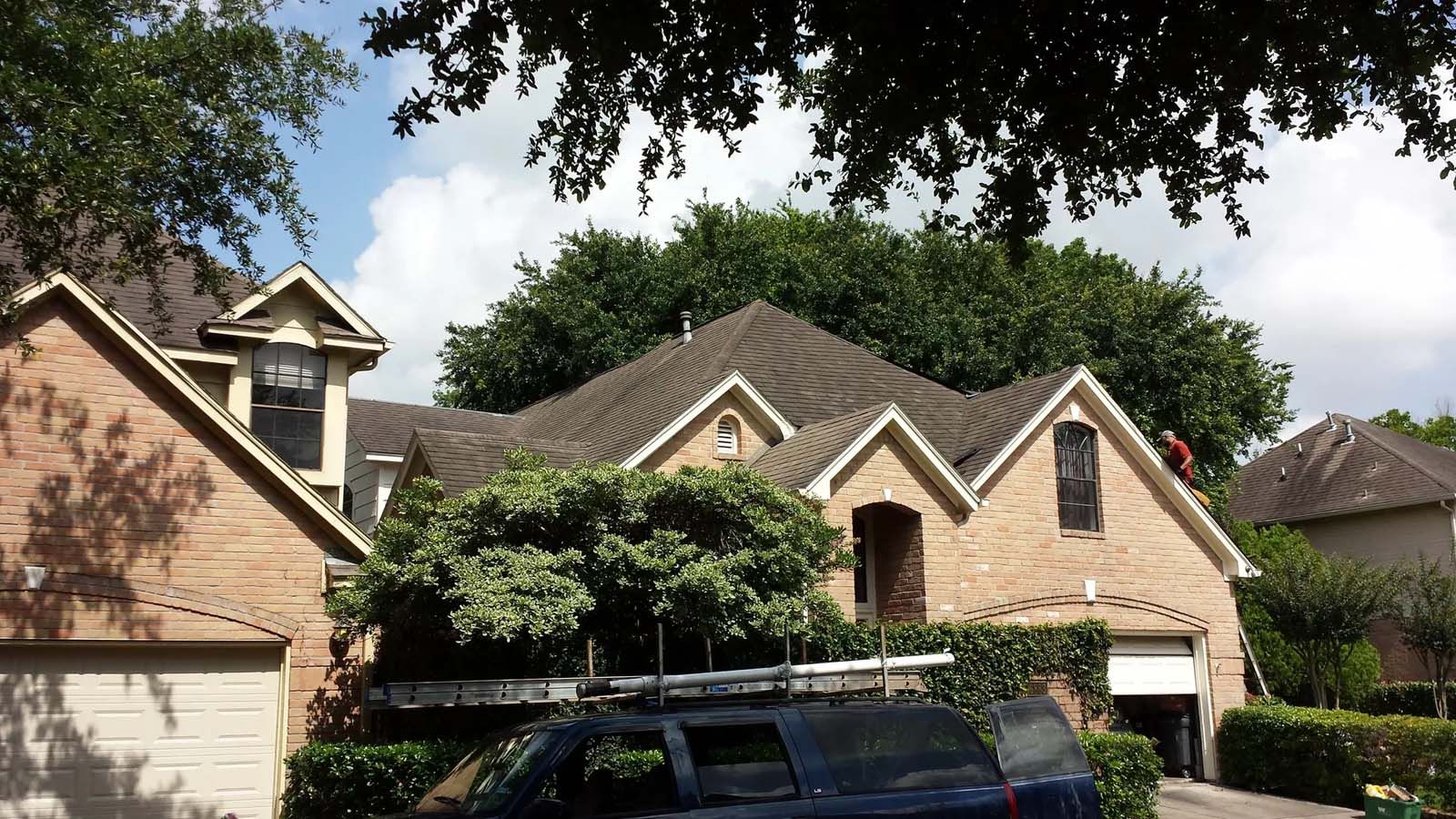 Suburban brick house with peaked roofs, trees, and parked cars in front