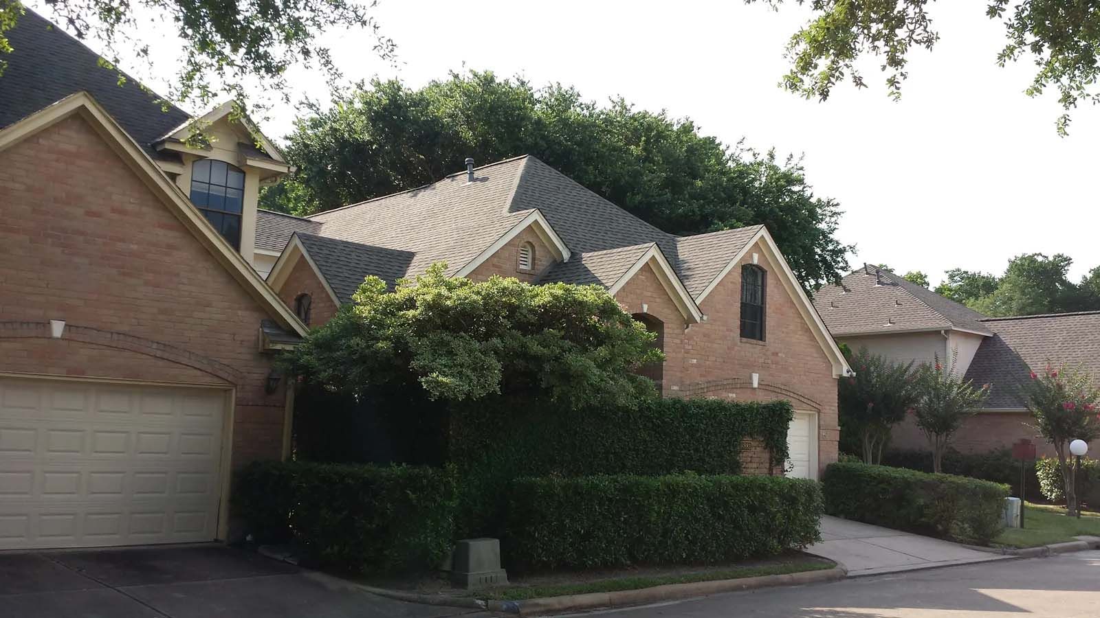 Brick suburban houses with garages and hedges along a quiet residential street