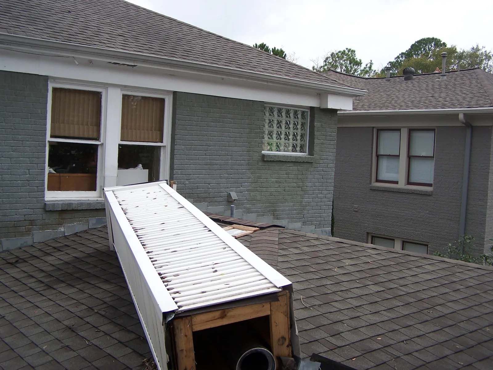 Rooftop with a small white ramp leading from an open skylight or hatch on a gray shingled roof.