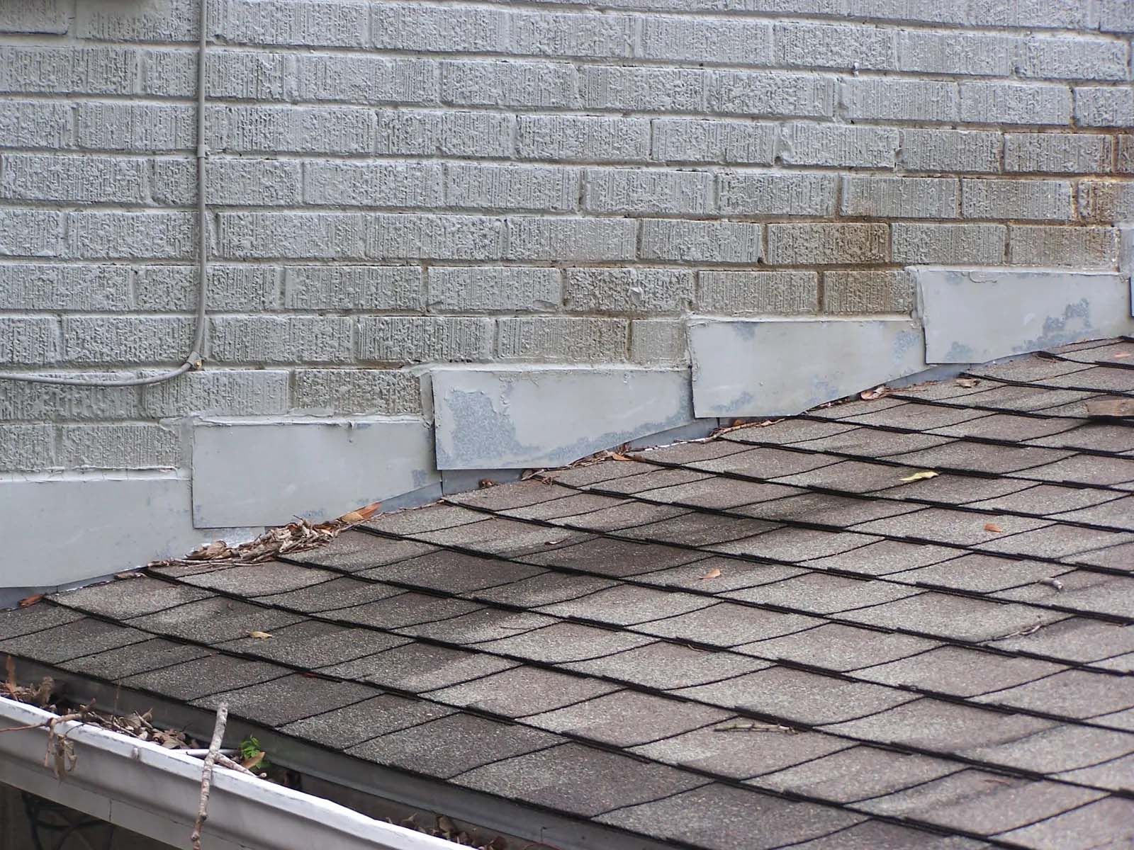 Roof shingles meeting a gray brick wall with metal flashing along the edge