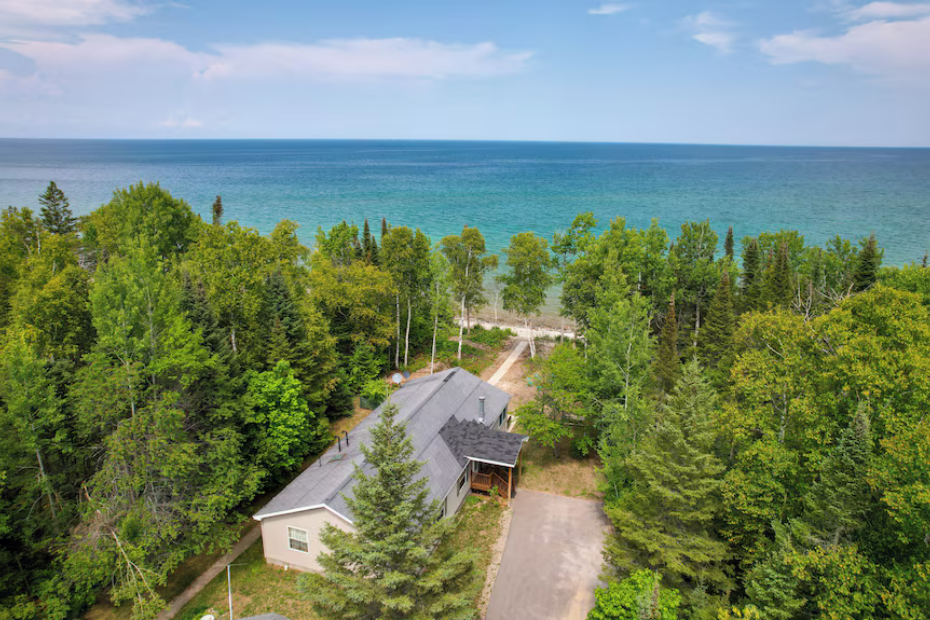 House nestled in green trees with a view of a blue lake under a bright sky.