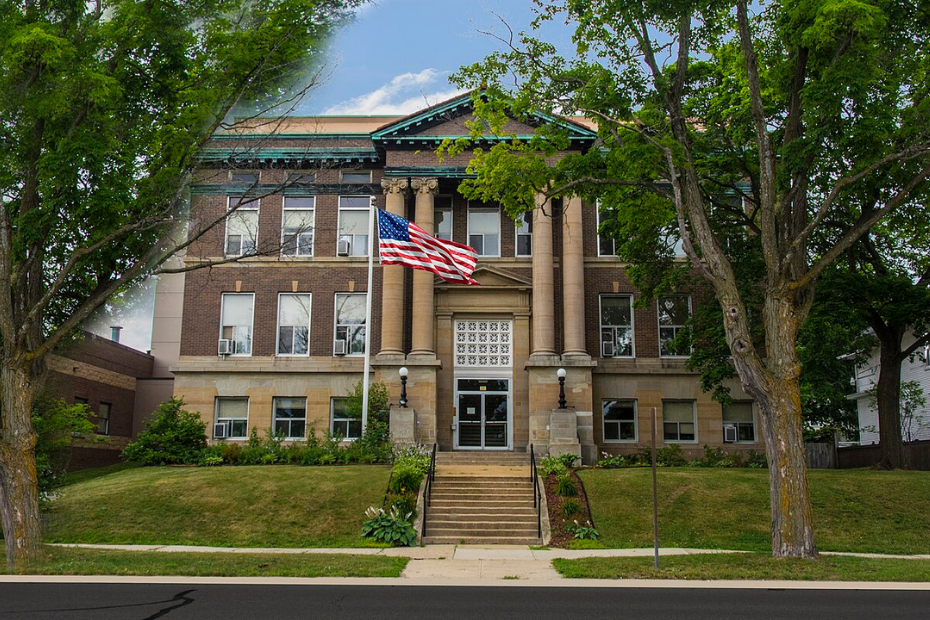 Brown brick building with columns and American flag, viewed from street.