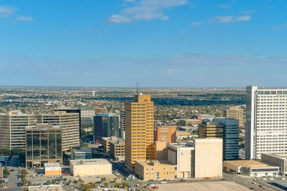 City skyline under a clear blue sky; buildings of varying heights and colors in the distance.