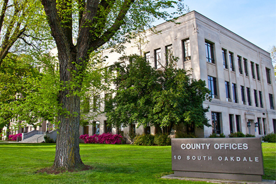 County Offices building in white stone with green lawn and trees, sign: 10 South Oakdale.