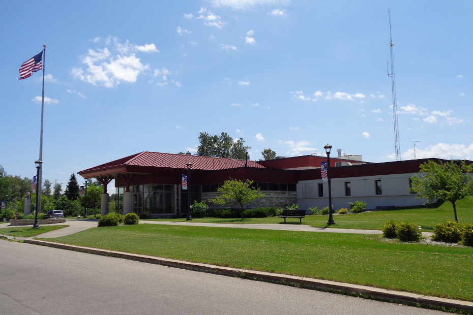 Building with red roof, US flag, green grass, and blue sky.