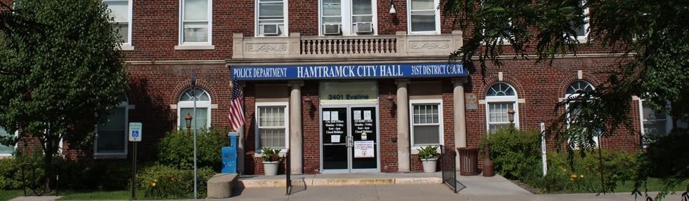 Front of the city hall building with an American flag and blue sign.