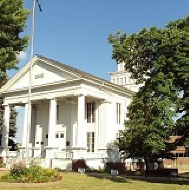 White courthouse building with columns, green trees, and blue sky.