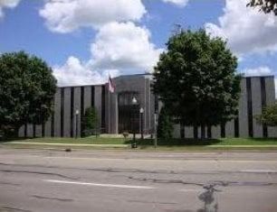 Exterior of a dark gray building with vertical stripes; trees and a cloudy sky visible.