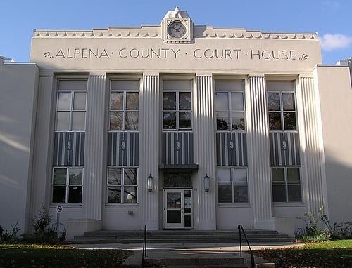 Alpena County Courthouse, a white art deco building with vertical columns and clock on the facade.