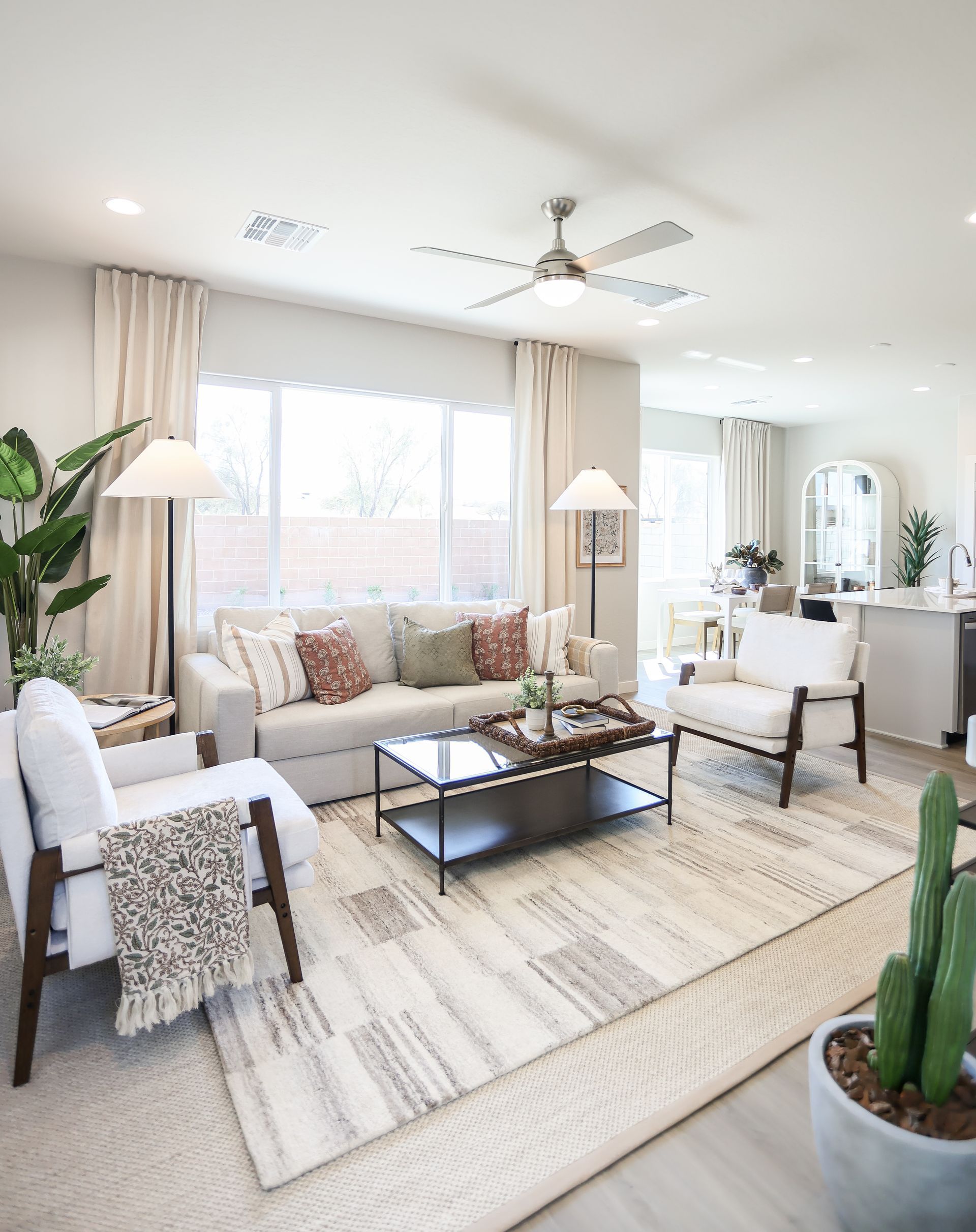 Bright living room with white furniture, large window, beige rug, and potted plants