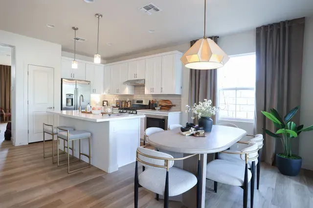 Bright open kitchen and dining area with white cabinets, island stools, round table, and large window.