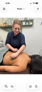 A massage therapist uses a gua sha tool on a client’s back in a serene treatment room.