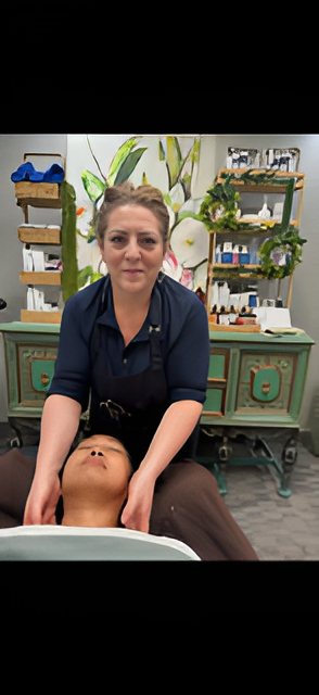 A spa professional performs a facial massage on a client lying on a treatment table in a wellness room.