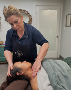 A therapist performs a gentle massage on a person's neck and shoulder area in a professional, serene treatment room.