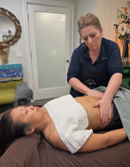 A professional massage therapist provides a gentle abdominal massage to a client lying on a treatment table.