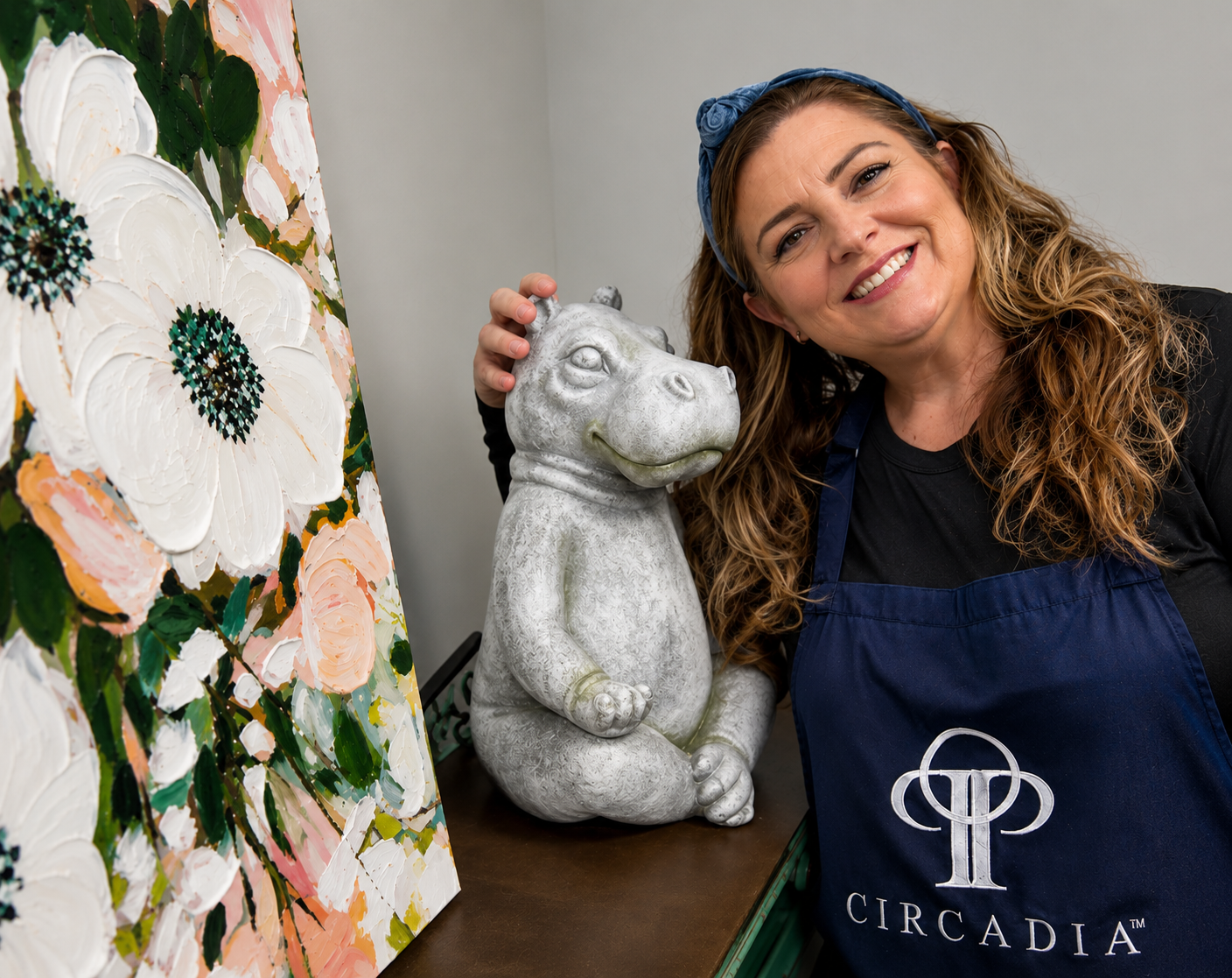 A person in a black apron with a Circadia logo poses next to a hippo statue and a floral painting.