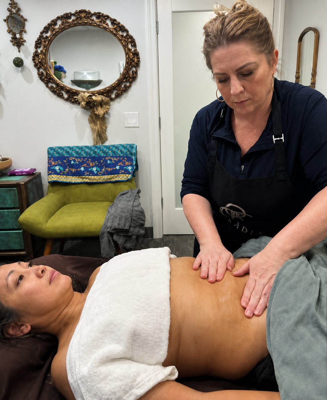 Hands massaging a person's abdomen, partially covered by a towel, lying on a massage table.