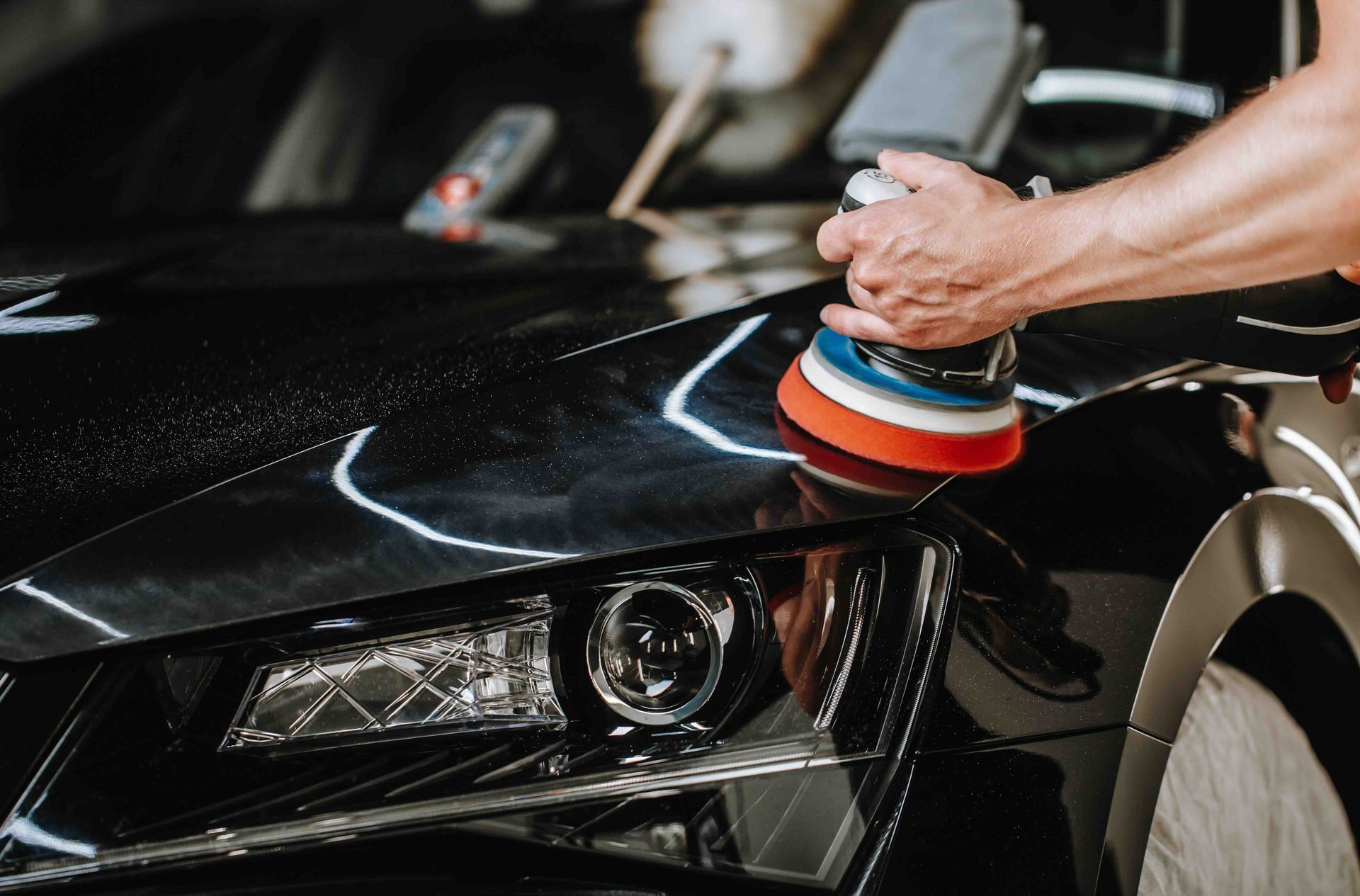A man is polishing a black car with a polisher.