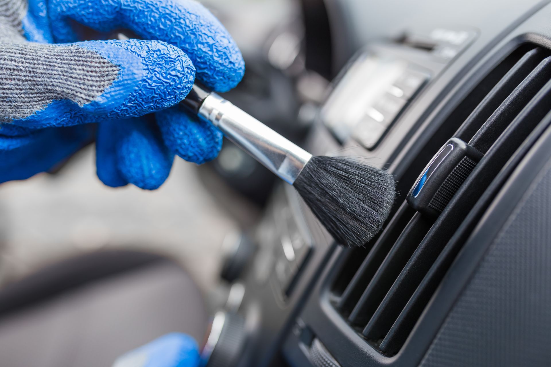A person is cleaning the air vents of a car with a brush.