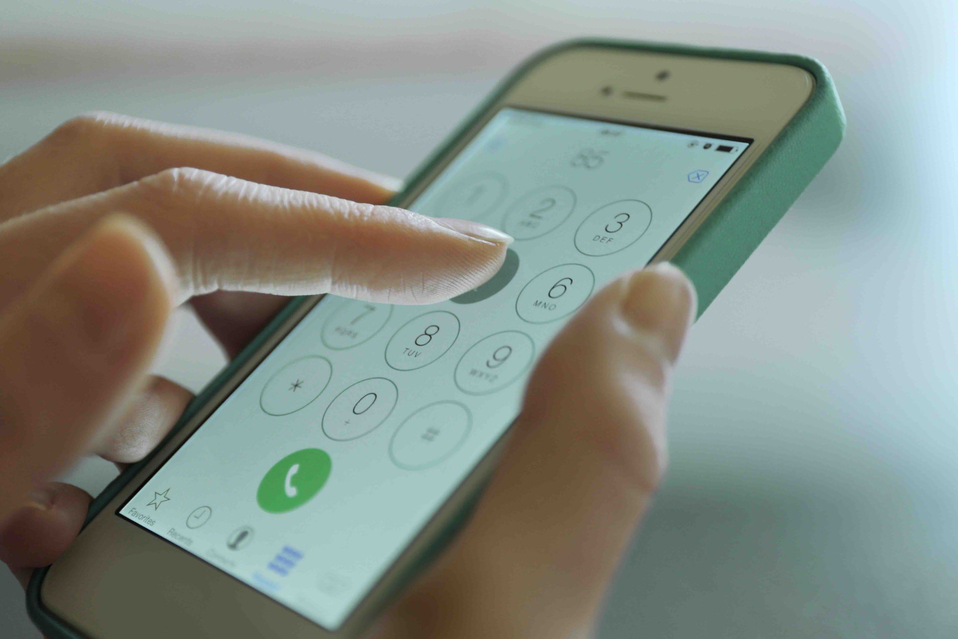 Person using a smartphone dialer, dialing a number with a finger. Phone is in a green case.