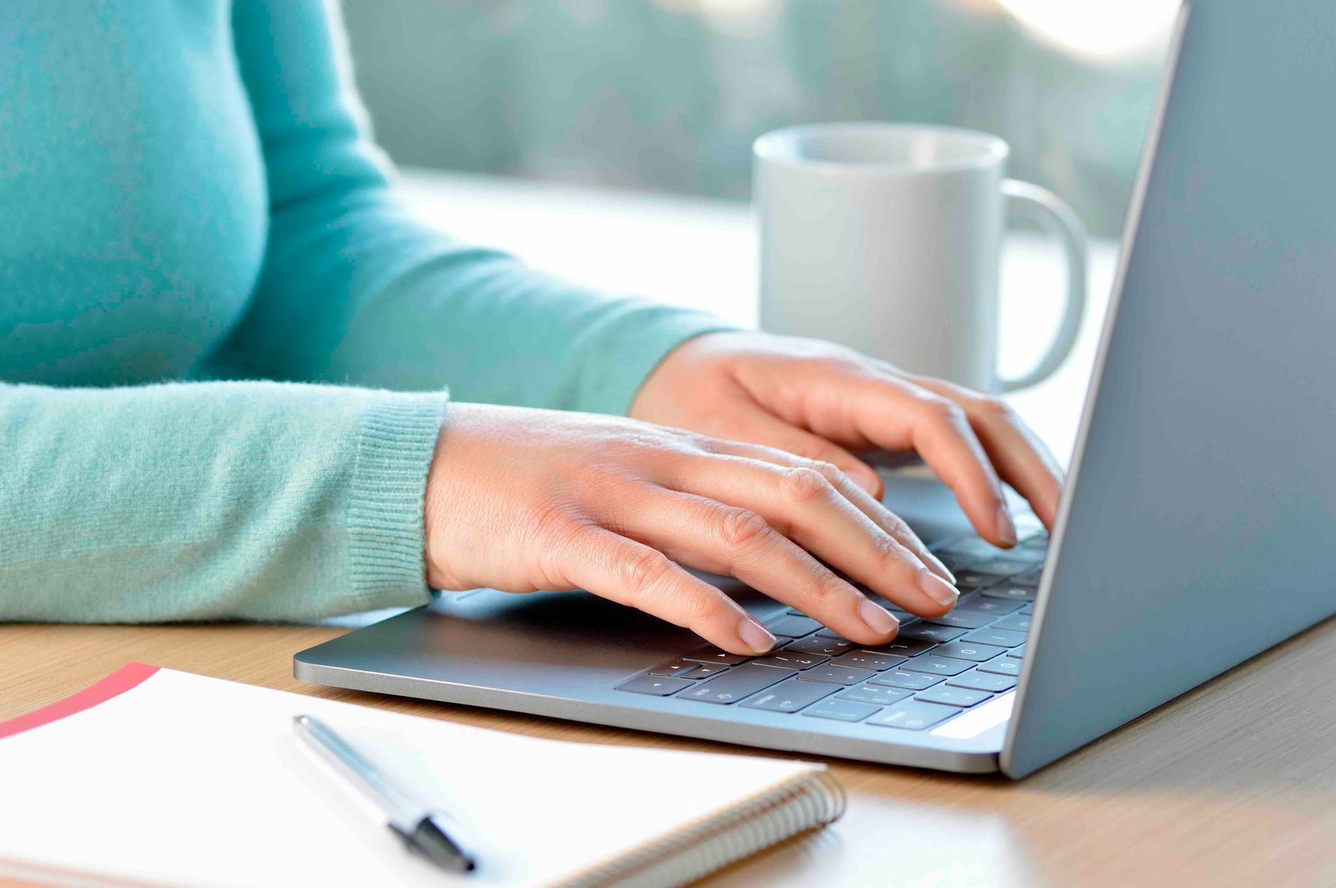 A woman is typing on a laptop computer next to a cup of coffee.