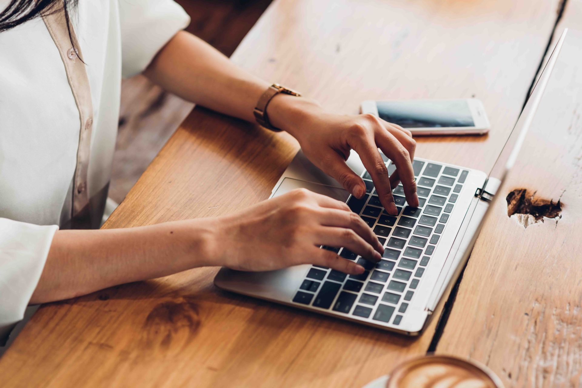 A woman is typing on a laptop computer while sitting at a wooden table.