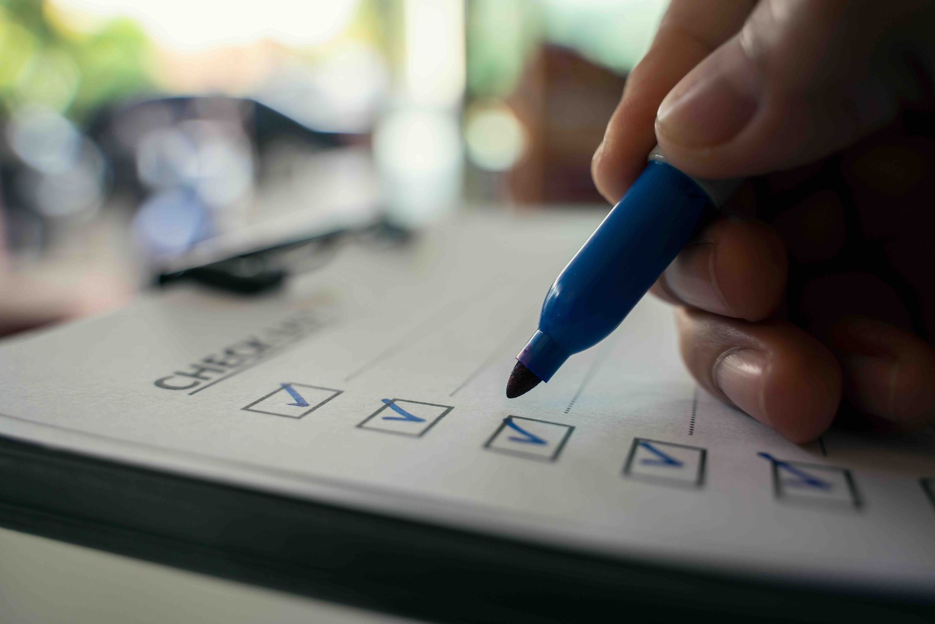 Hand with blue marker checks boxes on a checklist, close up.