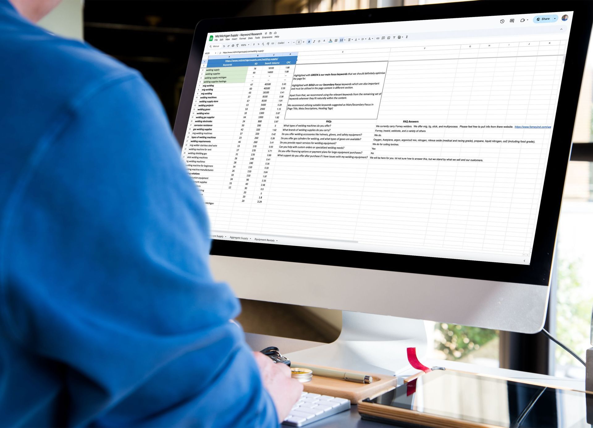 A man is sitting at a desk using a computer to search keywords for a website.
