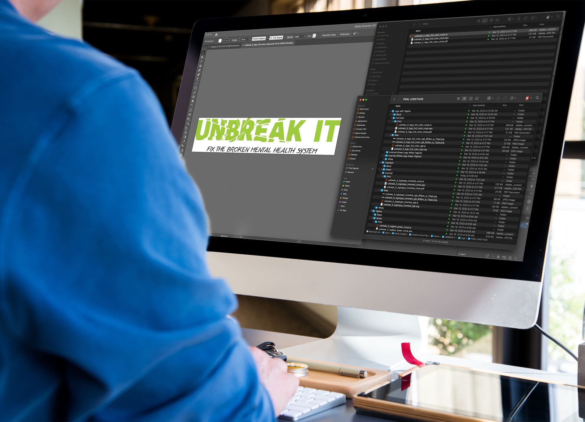 Person in blue shirt viewing a desktop monitor showing “UNBREAK IT” and code in a workspace.