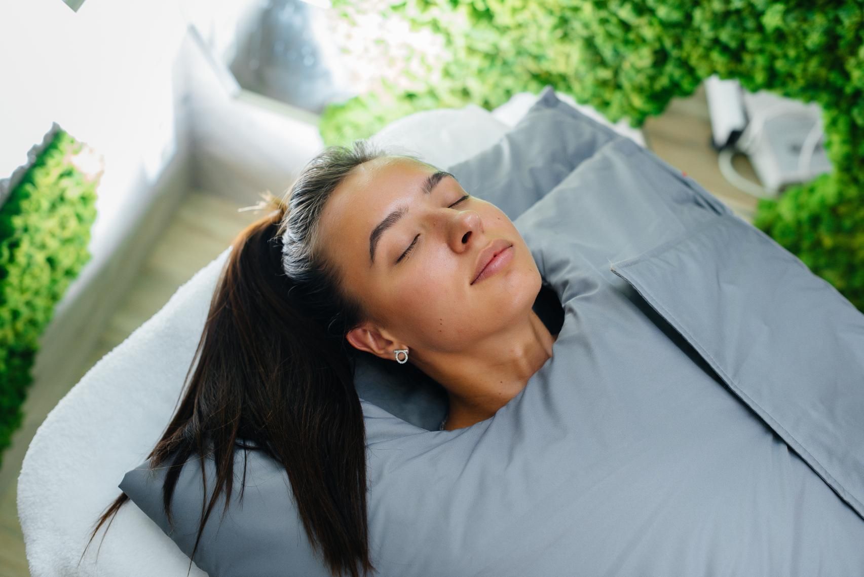 A Woman is Laying in a Blanket on a Bed With Her Eyes Closed — Xtreme Rejuvenation Clinic, Medispa & Beauty Therapy In Maryborough, QLD