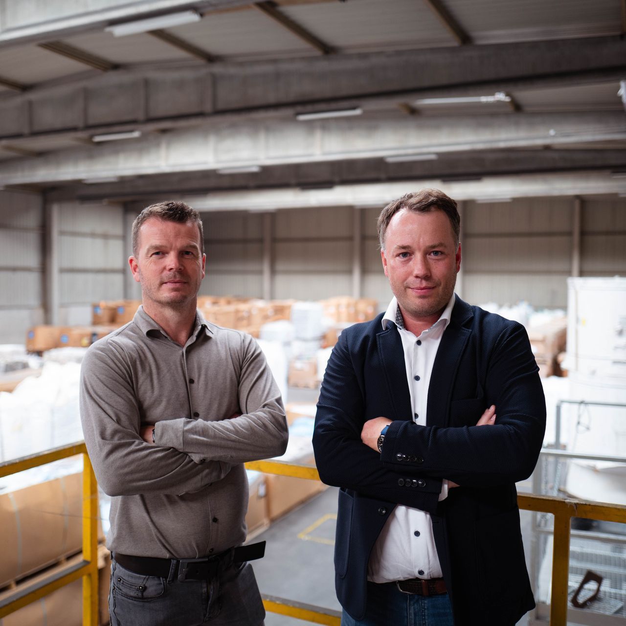 Twee mannen staan ​​naast elkaar in een pakhuis met hun armen over elkaar.