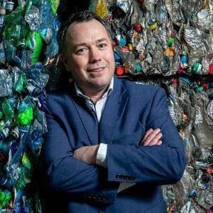 Een man in pak staat voor een stapel plastic flessen.